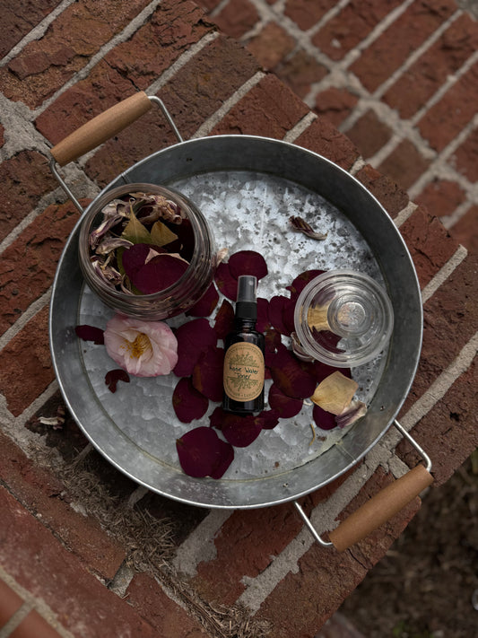 Metal tray with rose petals, a bottle, and a glass on a brick surface At The Salt and Light House