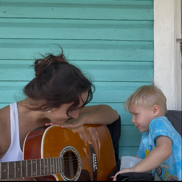 Woman playing guitar with a child on a teal wooden porch