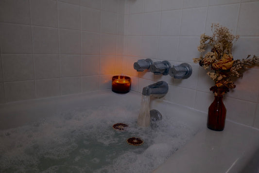 Bath tub with bubbles, oatmeal bath sachet, candle, and flowers in a bathroom setting